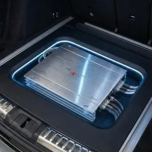 Installatie van een autoradioversterker met een zilveren versterker met blauwe LED-accentverlichting gemonteerd in de kofferbak van het voertuig.