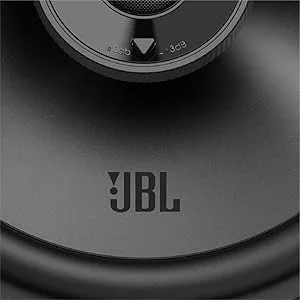 De tekst luidt 'JBL'. Macro-opname van dichtbij van zwart luidsprekeroppervlak met JBL-branding in een donkere, minimalistische setting.