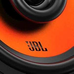 De tekst luidt „JBL”. Close-upopnamen van wat lijkt op een JBL-luidsprekercomponent met zwarte en oranje kleuren, met details van de luidsprekerconus.