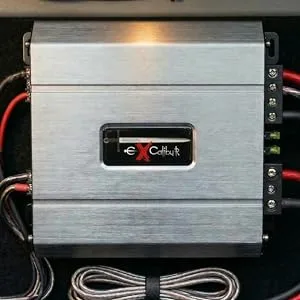 Auto-audioversterker met een zilverkleurig aluminium chassis gemonteerd, met rode en witte stroom-/signaaldraden die zijn aangesloten op de aansluitingen.
